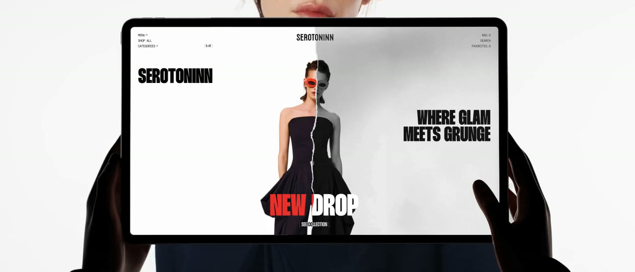 El sitio de Serotoninn abierto en una tableta que alguien sostiene con las dos manos. En pantalla, la portada de la tienda: el nombre de la marca a la izquierda, «where glam meets grunge» a la derecha, una modelo al centro partida en dos mitades —una en color y otra en gris— y la línea de campaña «new drop» en rojo al pie.