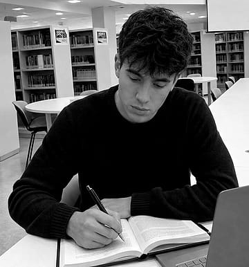 Thiago escribiendo a mano en la sala de lectura de una biblioteca.